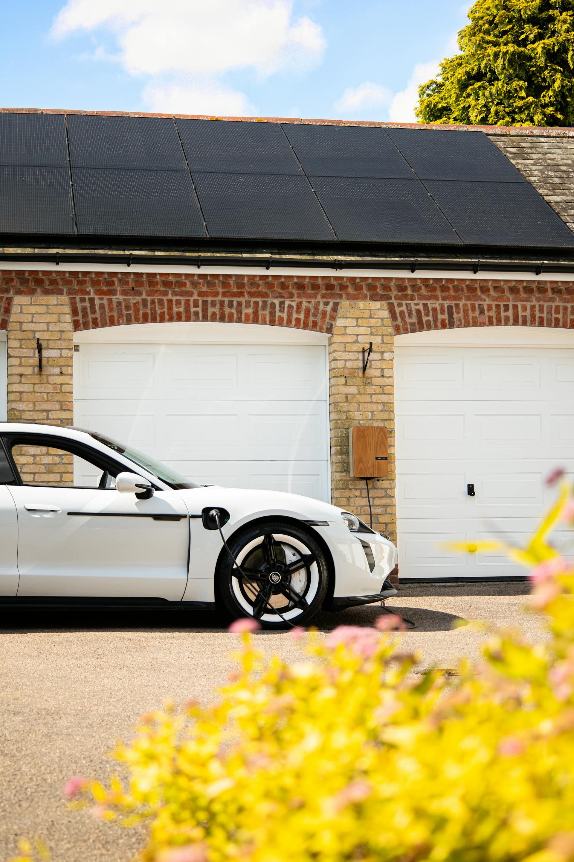 Weißes Elektroauto lädt an einer Wallbox vor einem Haus mit Solaranlage